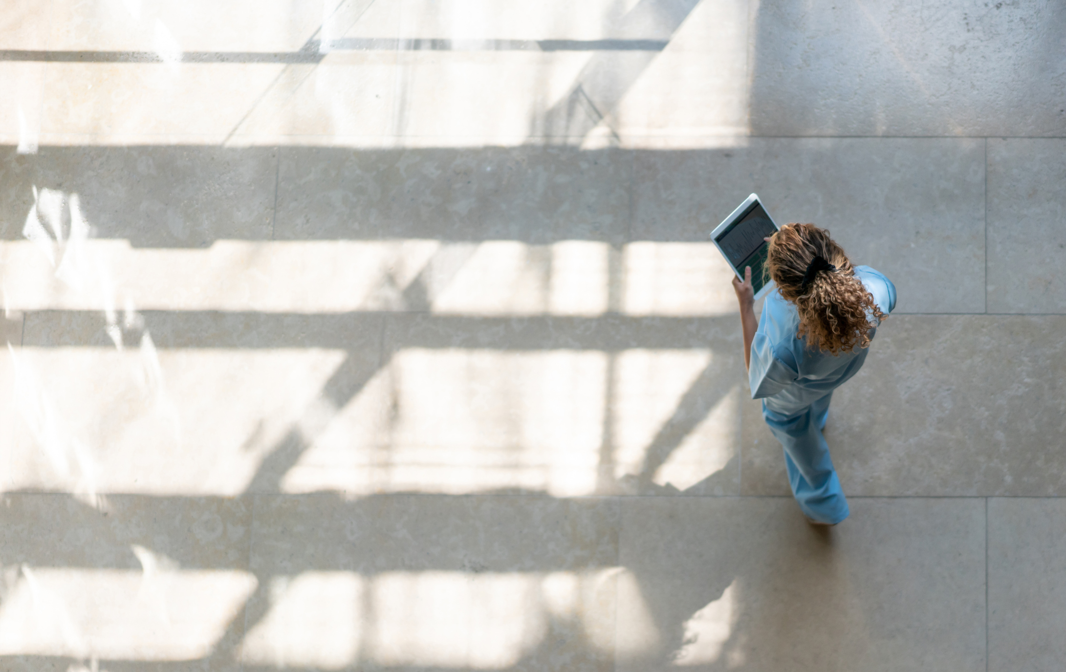 High angle view of nurse walking walking around hospital while looking at a medical chart on tablet