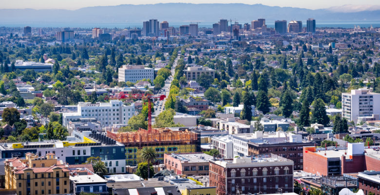 Aerial view of Berkeley and north Oakland on a sunny day; downtown Oakland in the background; buildings in UC Berkeley in the foreground; San Francisco bay, California